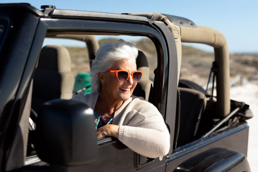 ältere frau mit sonnenbrille fährt in einem offenen jeep am strand